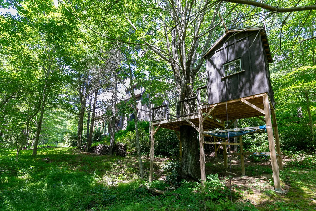An exterior shot of a charming treehouse nestled among mature trees, surrounded by open space and greenery. The scene radiates a playful, adventurous mood, showing a spot perfect for supervised children to explore, dream, and build lasting memories.