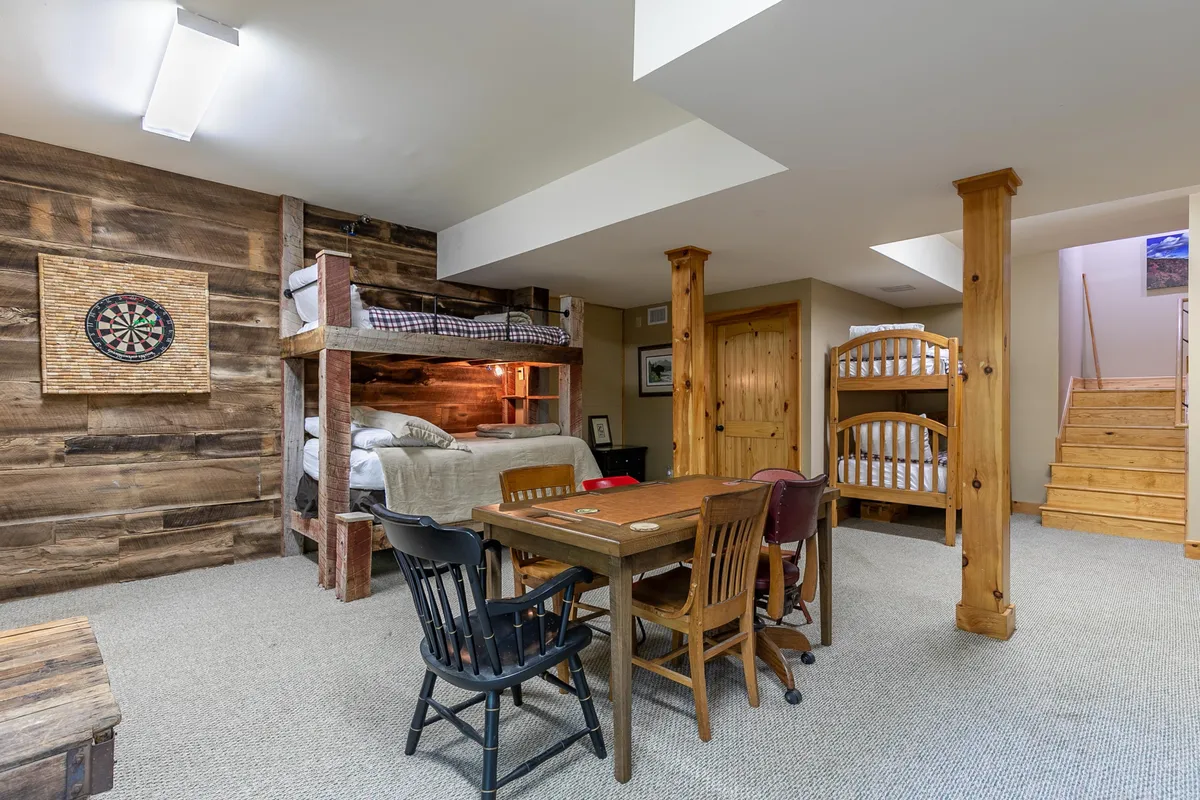 Inside, the warm game room is equipped with cozy bunk beds, a dining table perfect for board or card games, and a dartboard on the wall. The space is inviting for children and families to gather, play, and make memories, especially on rainy or winter days.