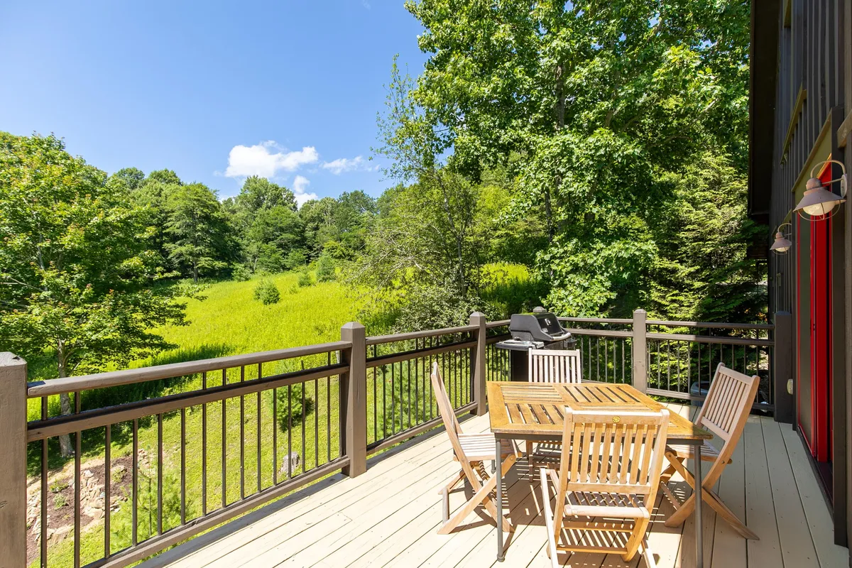 The spacious deck just off the main living area, featuring a wooden dining set, a grill, and lush greenery all around. The inviting setup is perfect for al fresco meals and relaxing while enjoying mountain breezes.