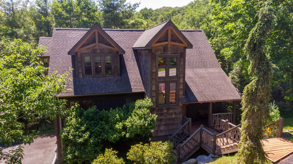This exterior image features the home's distinctive architectural design, welcoming front steps, and the lush greenery that surrounds the property. The house stands invitingly amidst its natural setting, with sunlight casting a warm glow on the façade and upper windows.