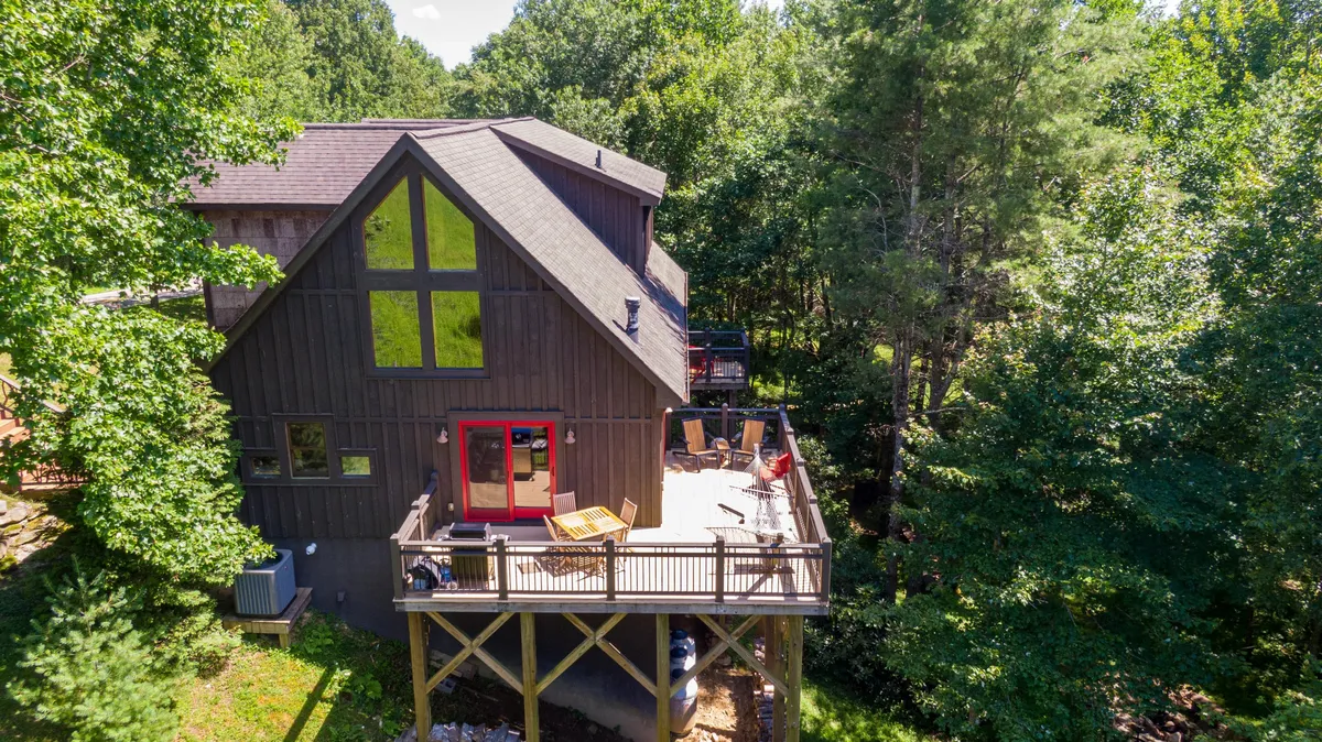 The expansive wooden deck attached to the house features comfortable seating and overlooks a scenic outdoor setting. Large windows connect the interior to the outdoors, while the deck is ready for outdoor meals or morning coffee, surrounded by peaceful mountain views.