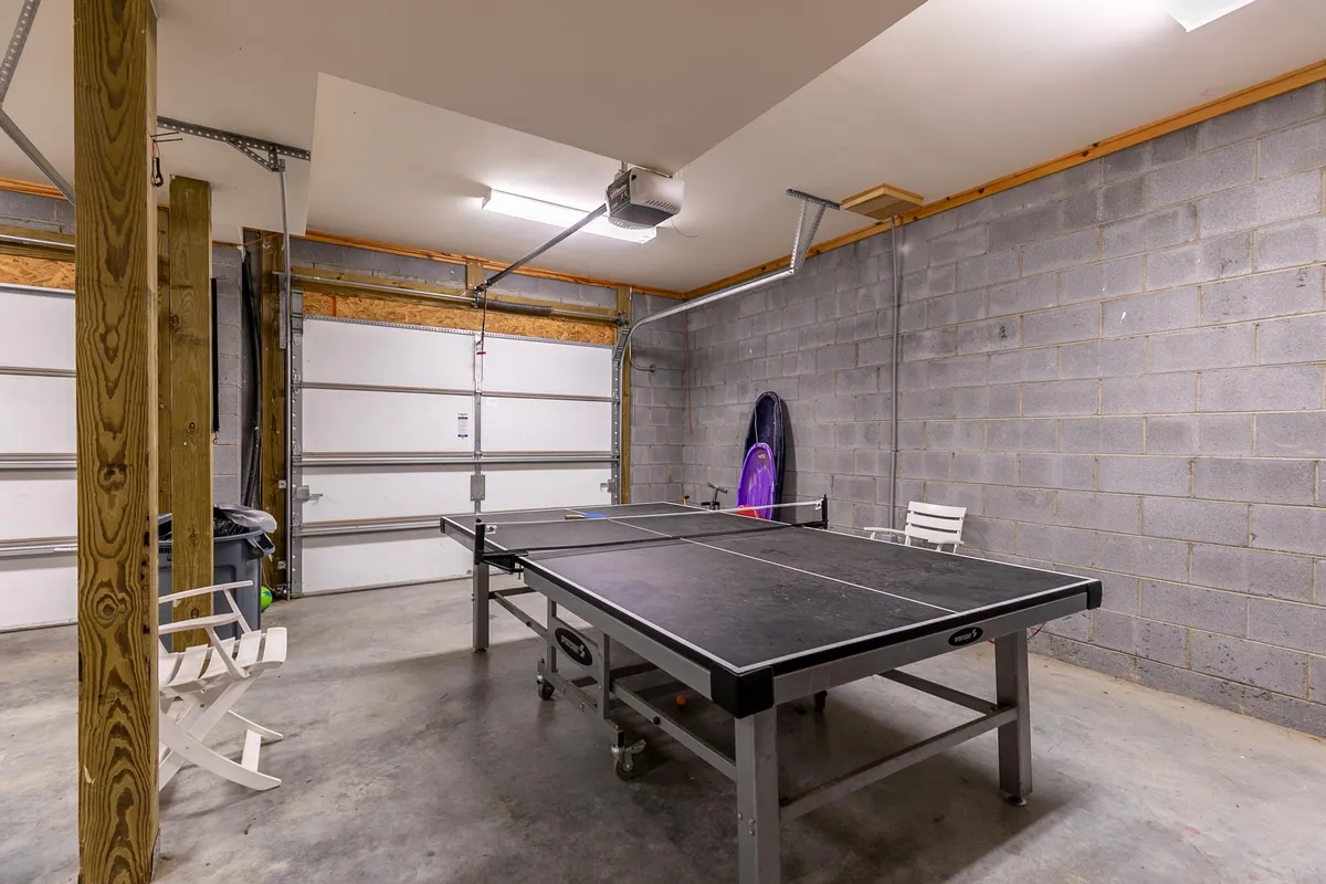 A view of the garage set up as a recreation area, highlighting a ping pong table ready for action. The space features garage doors and wooden support beams, with a casual, playful mood enhancing its role as a hub for friendly competitions and shared laughter.